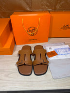 Hermes tan leather slide sandals with two wide straps and metal buckle, open toe.