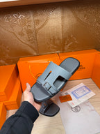 Hermes slide sandals in light blue-gray leather with front strap and silver buckle.