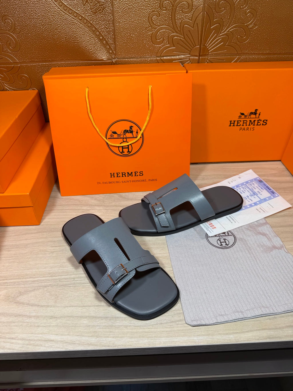 Hermes light blue-gray leather slide sandals with front cutout strap and square buckle.