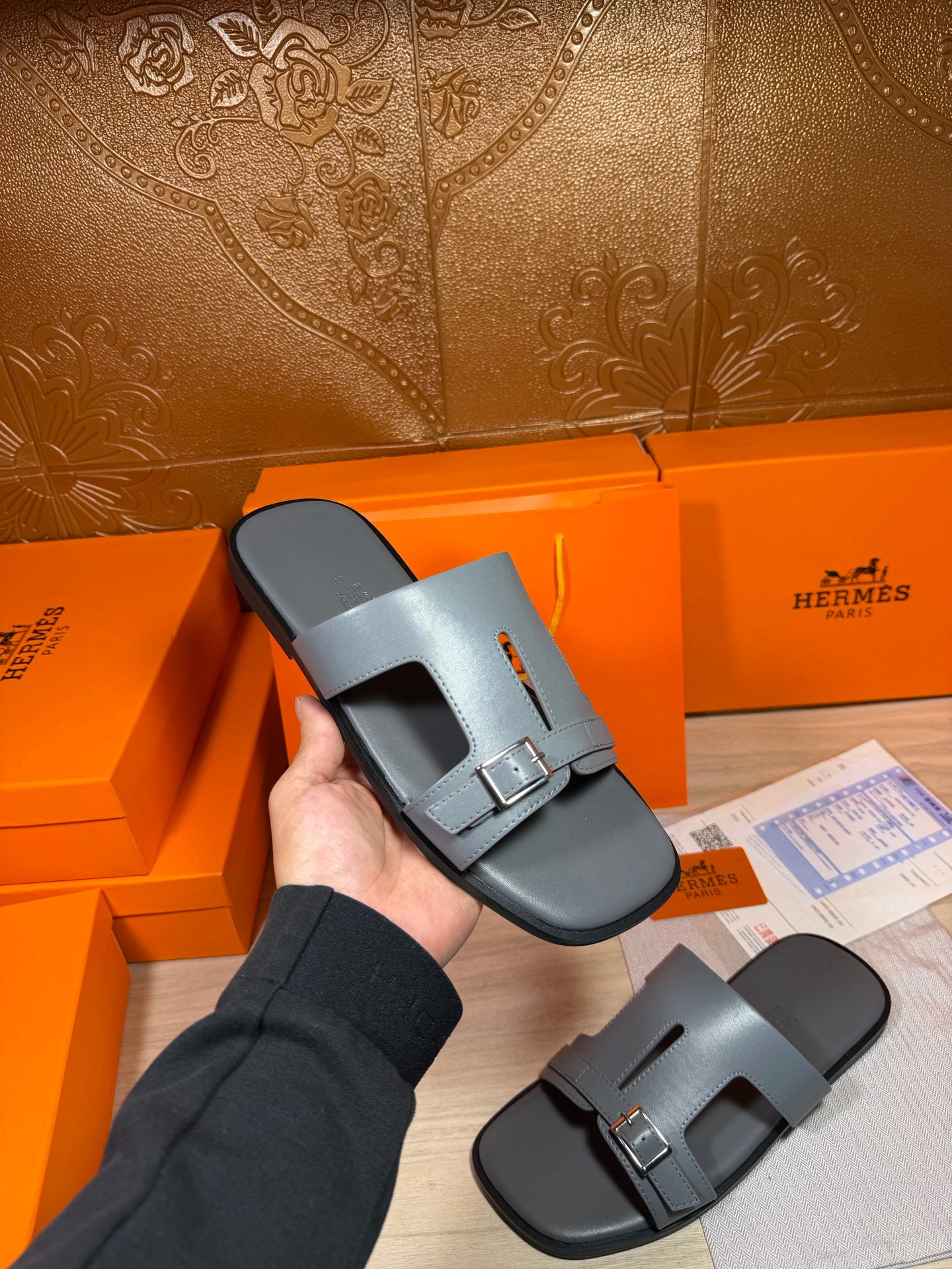 Hermes light blue-gray slide sandals held in hand; wide strap with silver buckle.