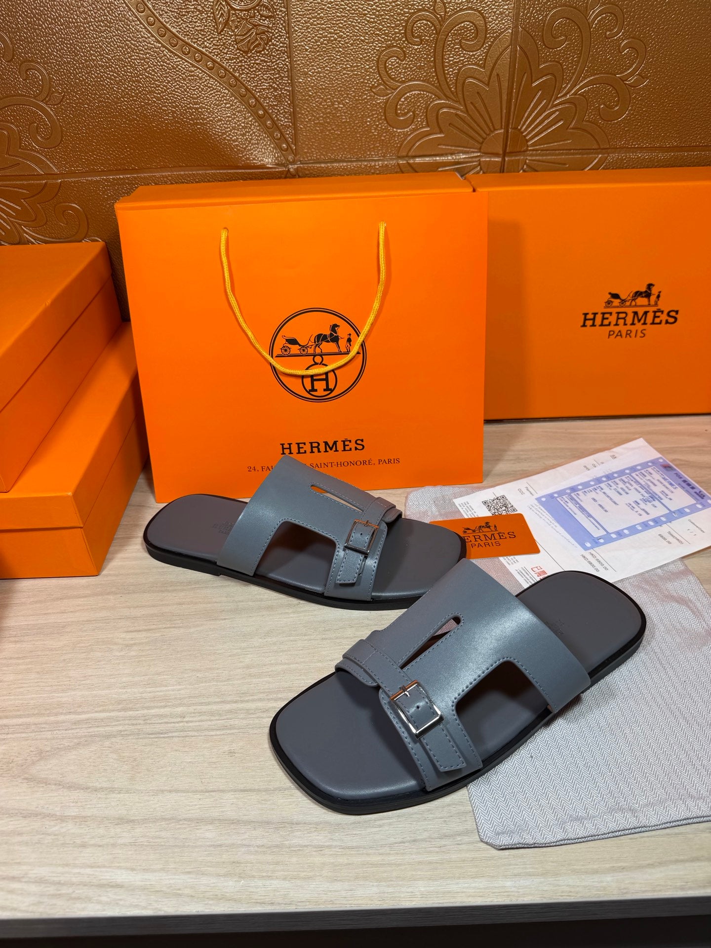 Pair of Hermes slide sandals in light blue-gray leather with wide strap and metal buckle.