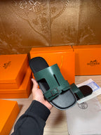 Hand holding Hermes sandals: teal strap with silver buckle on black footbed