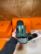 Hermes sandal held up showing teal strap with silver buckle and black sole