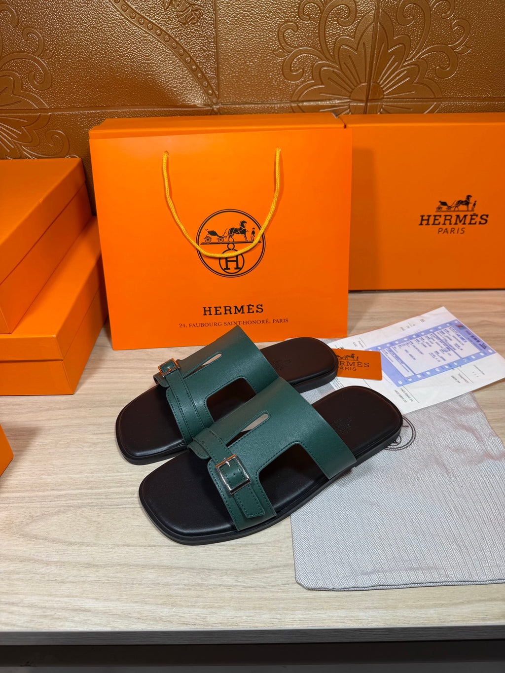 Hermes sandals shown at angle: teal slide strap over black footbed with buckle
