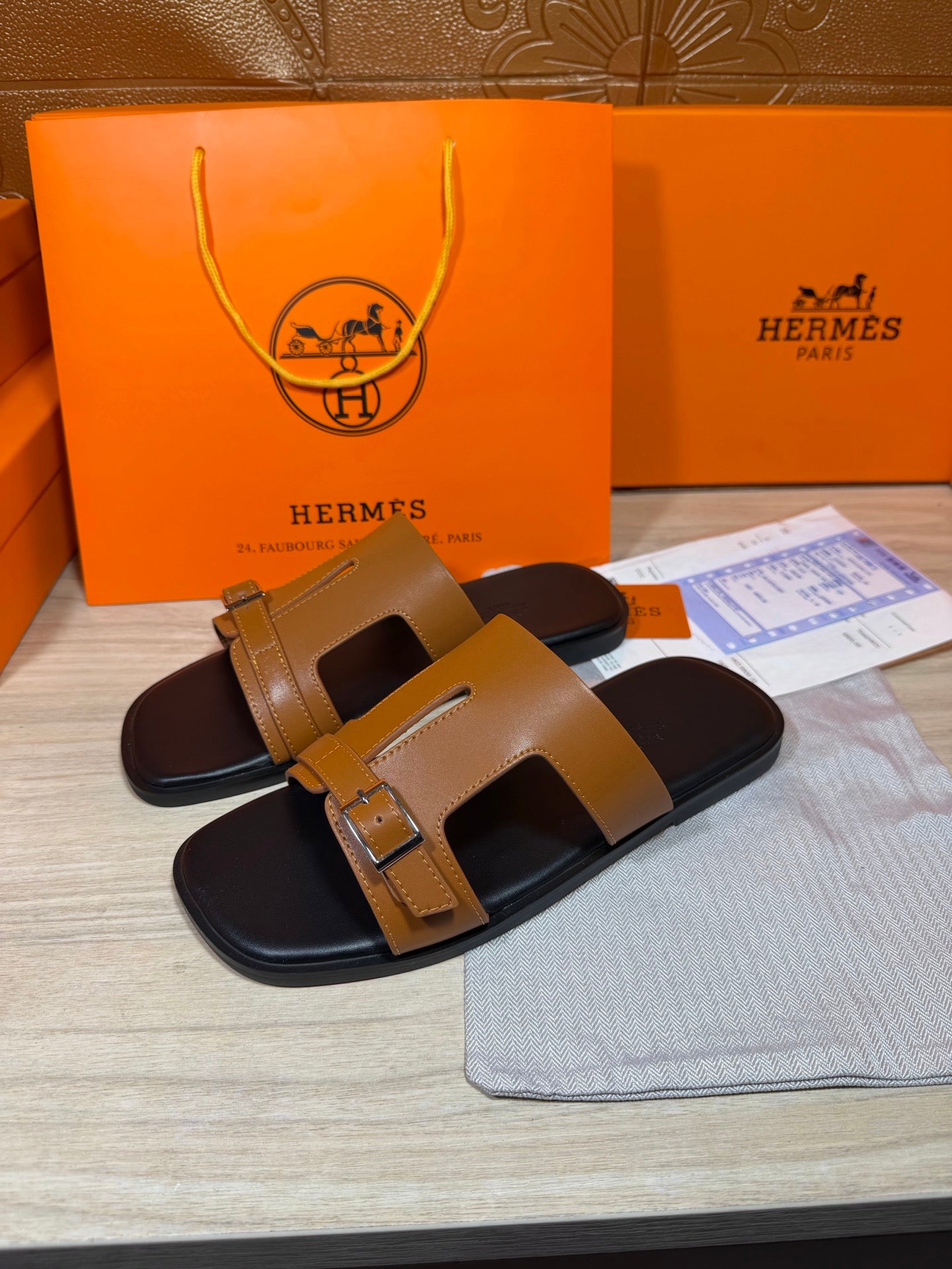 Tan and black leather slide sandals with wide front strap and buckle