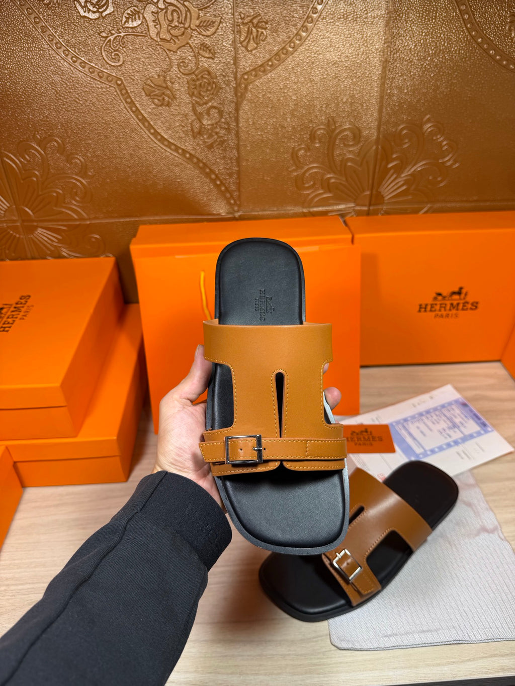 Tan leather slide sandal with two buckle points over dark footbed, held up