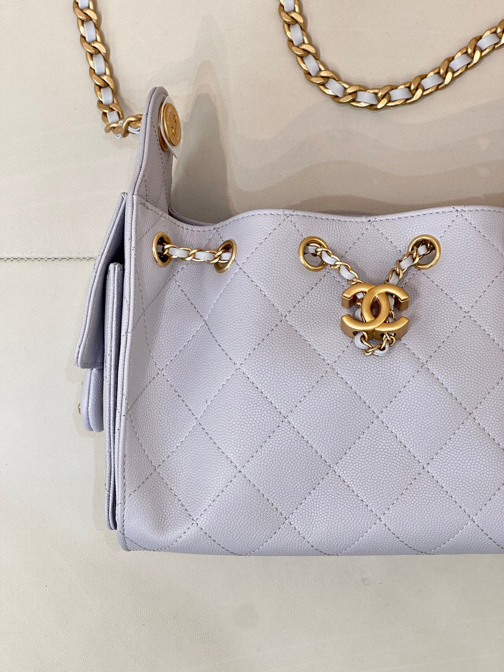 Light blue quilted handbag front with gold chain strap, rings, and Chanel logo charm