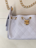 Light blue quilted handbag front with gold chain strap, rings, and Chanel logo charm