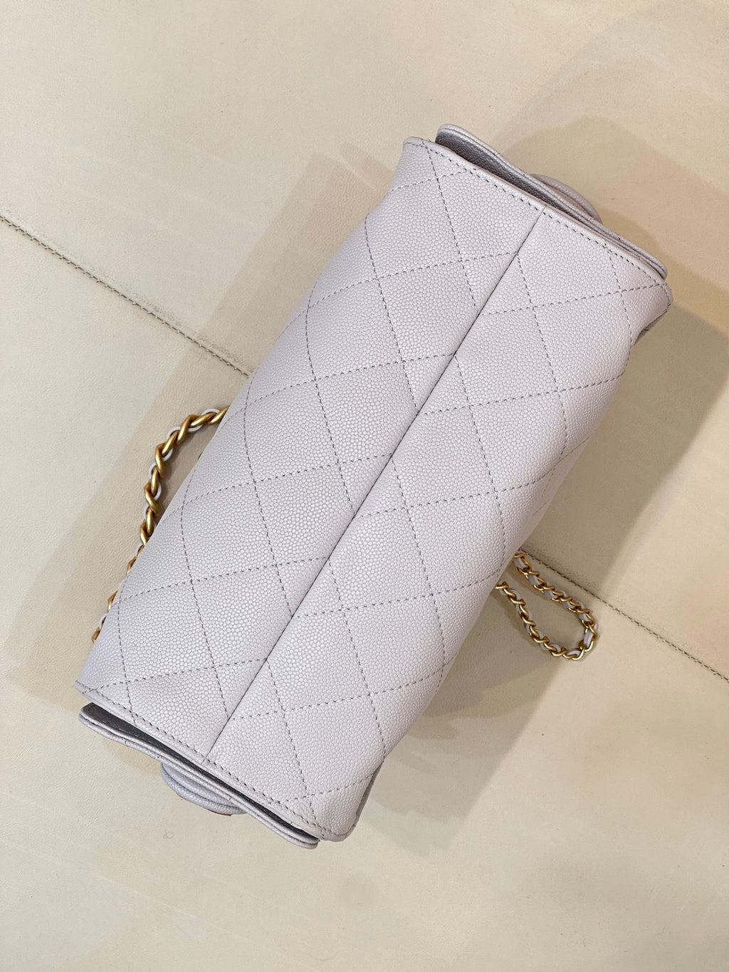 Light blue quilted handbag viewed from side, with gold chain strap and top edge