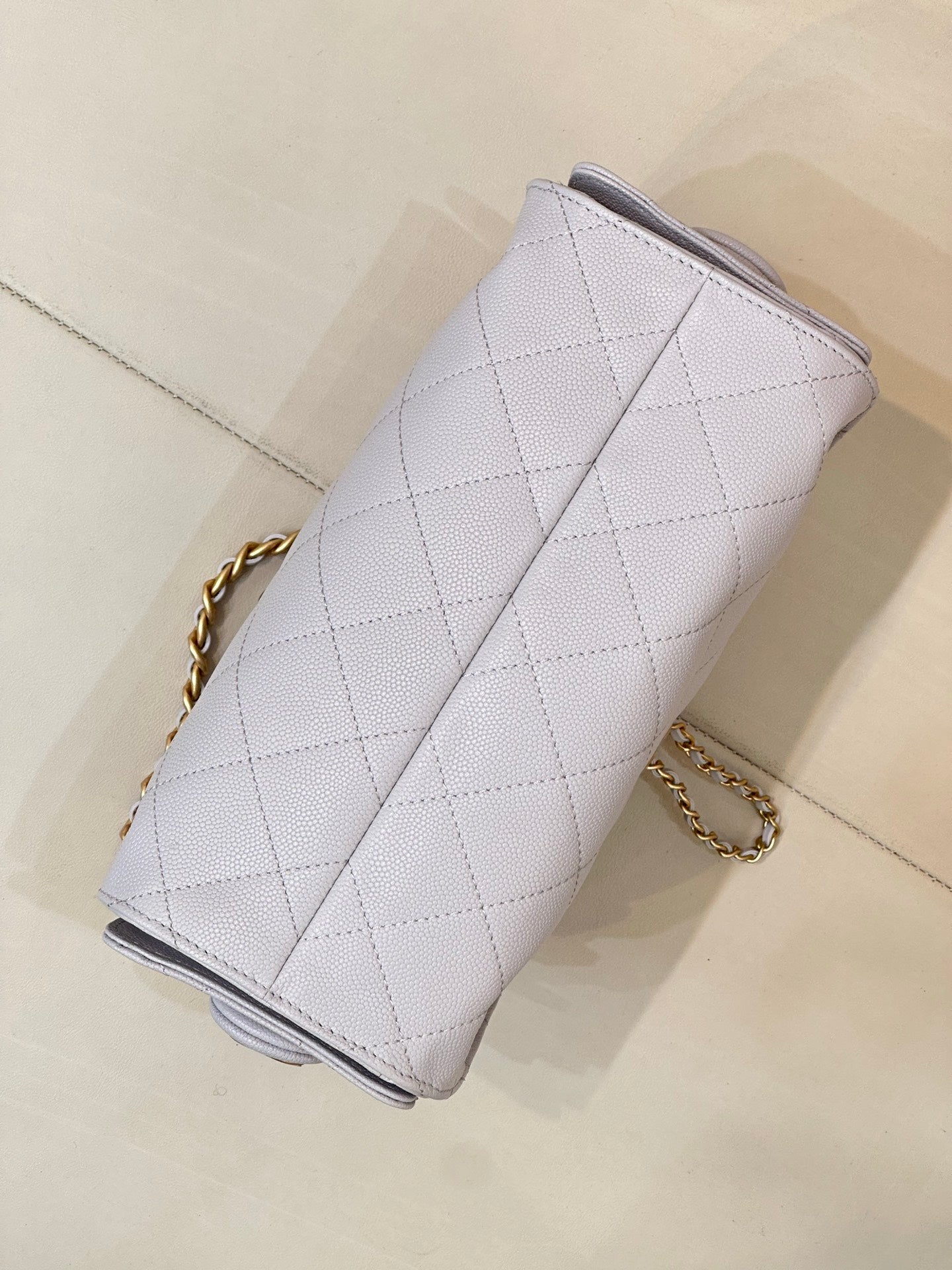 Light blue quilted handbag viewed from side, with gold chain strap and top edge