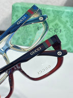 Gucci eyeglasses close-up: glossy temple logos with clear lenses on blue and maroon frames.