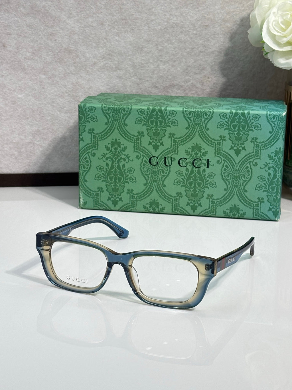 Gucci eyeglasses with dark frames and light blue temple accents; green logo case.