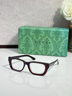Gucci eyeglasses with dark maroon frames and clear lenses; green logo case.