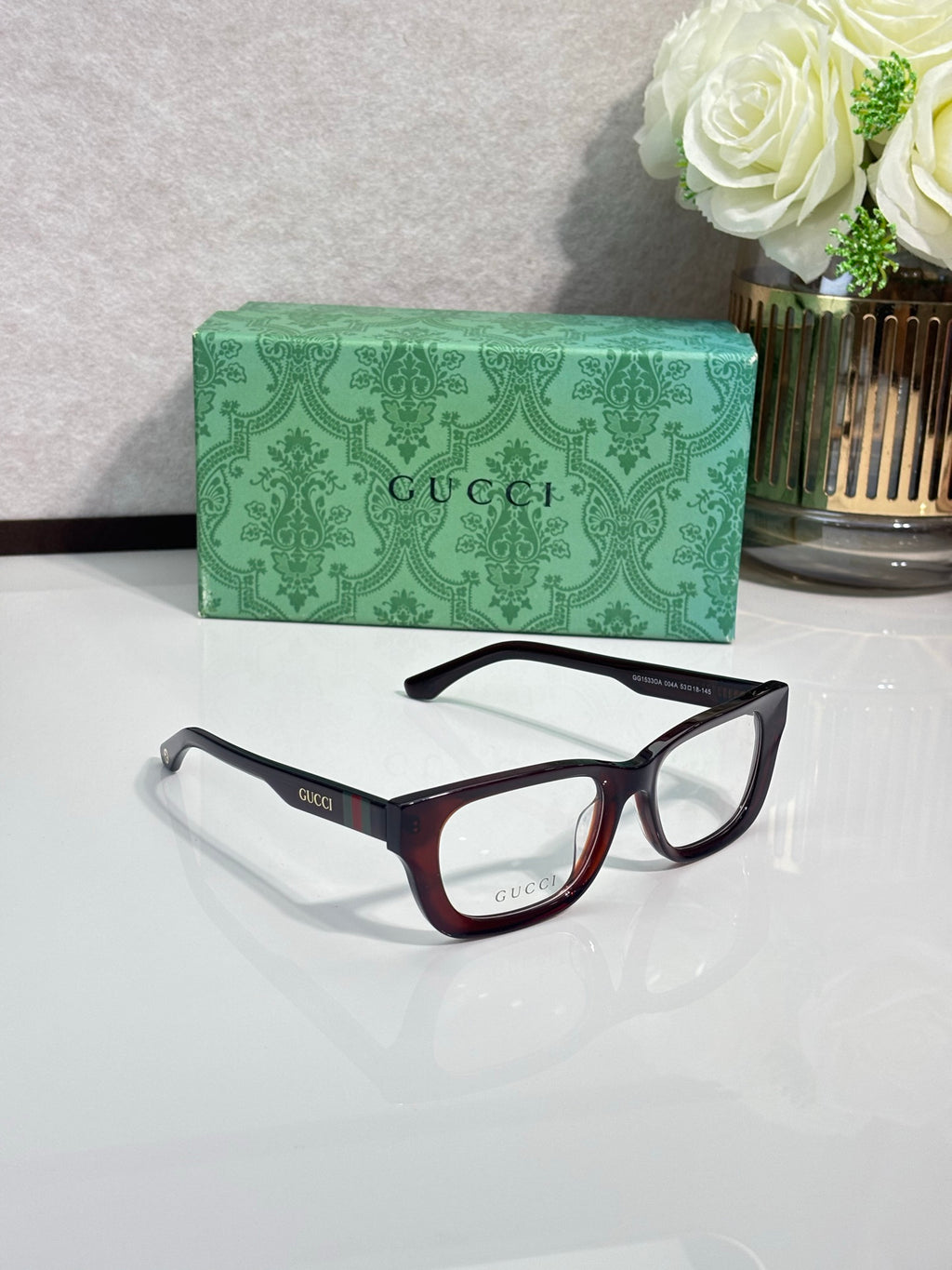 Two Gucci eyeglasses with maroon and black frames and clear lenses; green case.