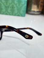 Gucci eyeglasses close-up of tortoiseshell temple with logo; clear lens rim visible.