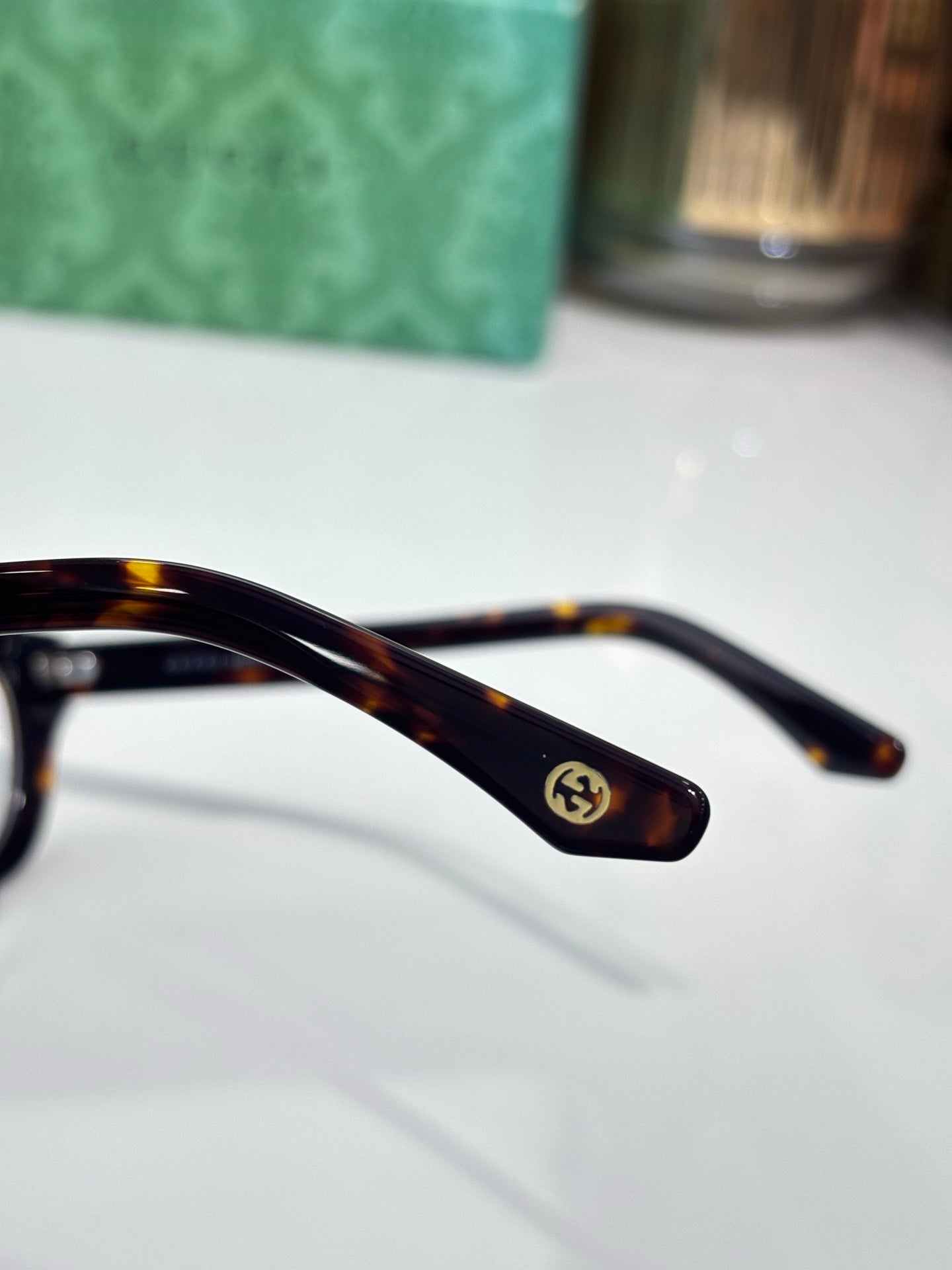 Gucci eyeglasses close-up of tortoiseshell temple with logo; clear lens rim visible.