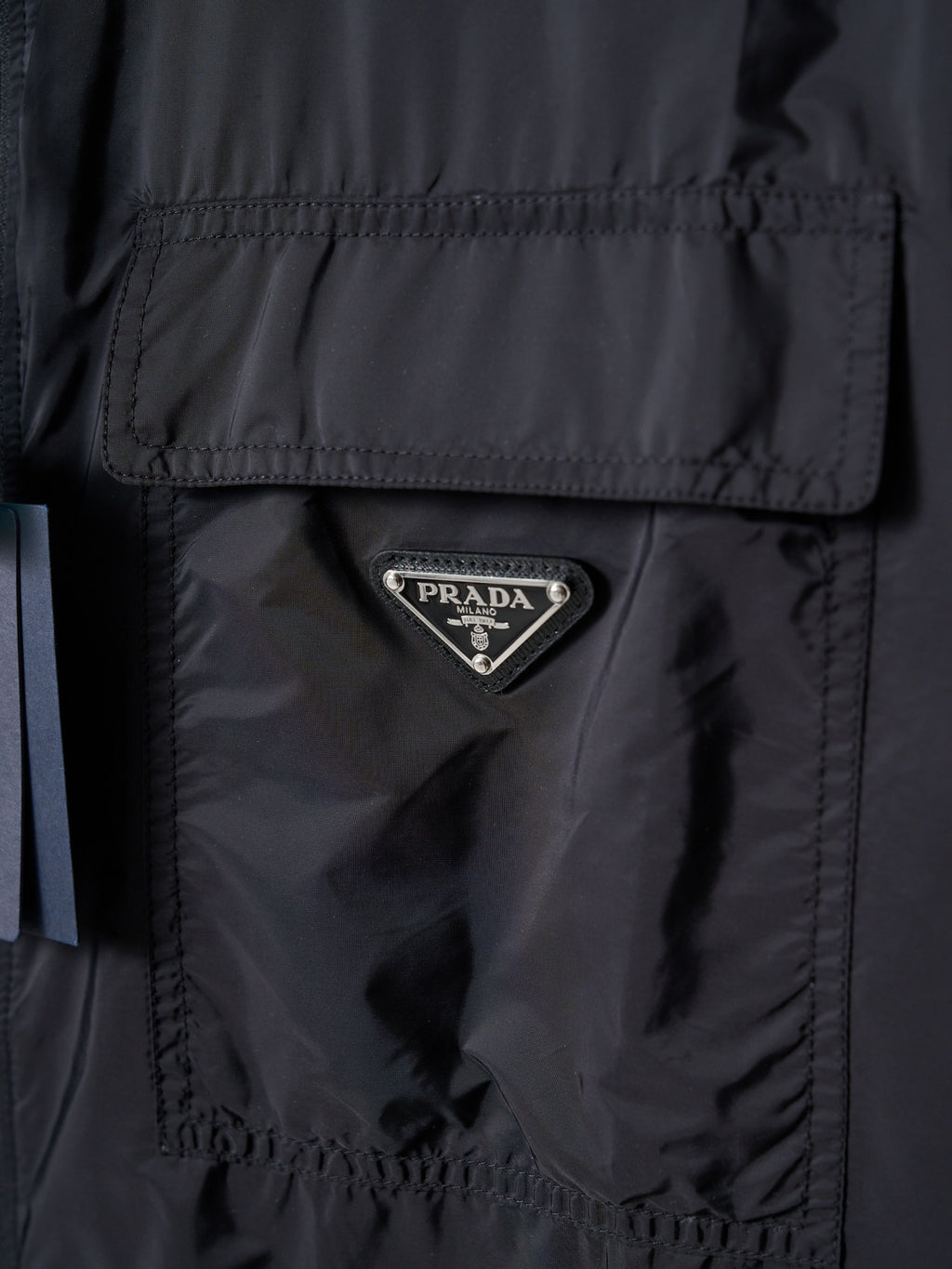 Prada dark jacket close-up of triangular Prada logo patch