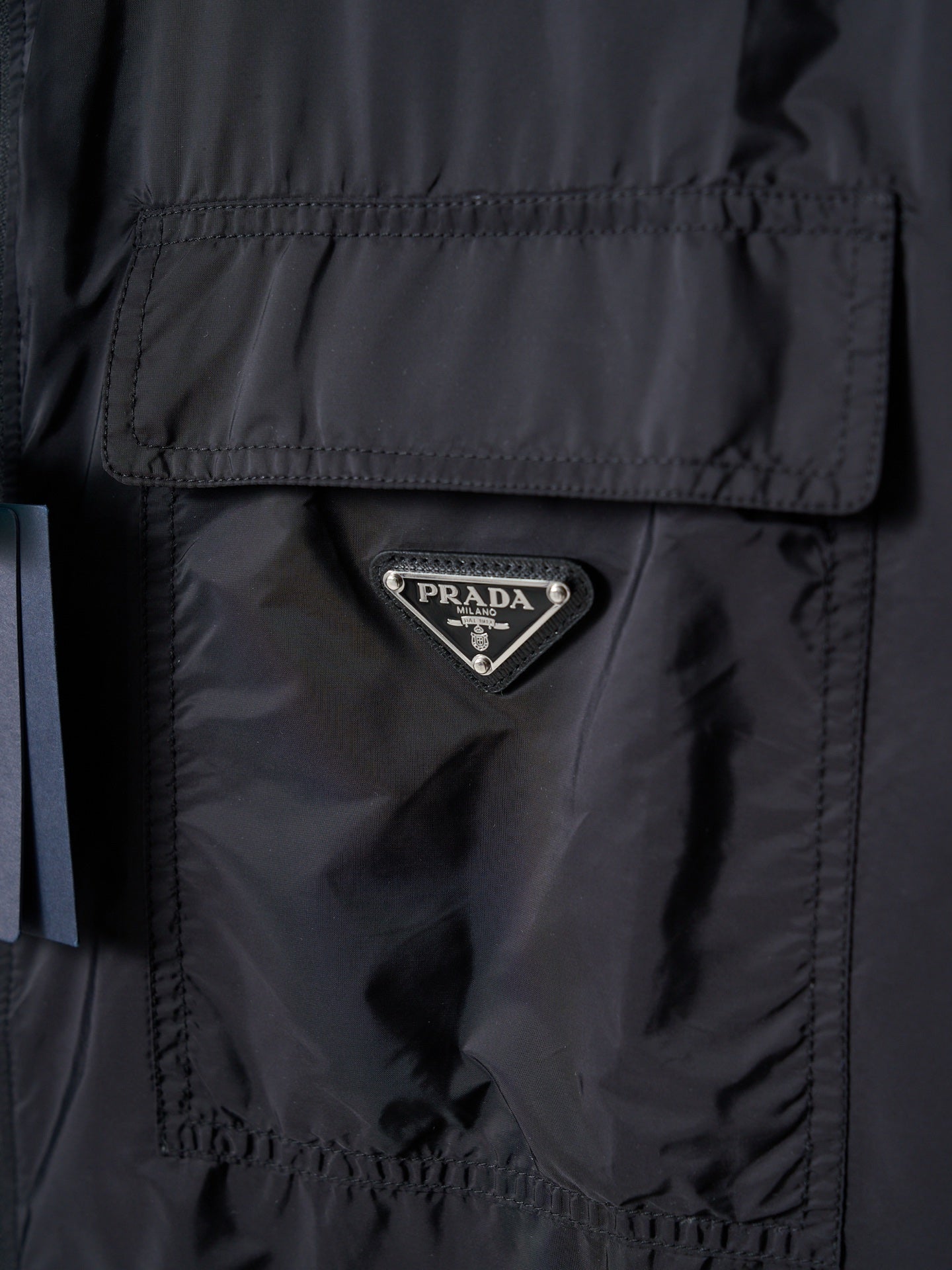 Prada dark jacket close-up of triangular Prada logo patch