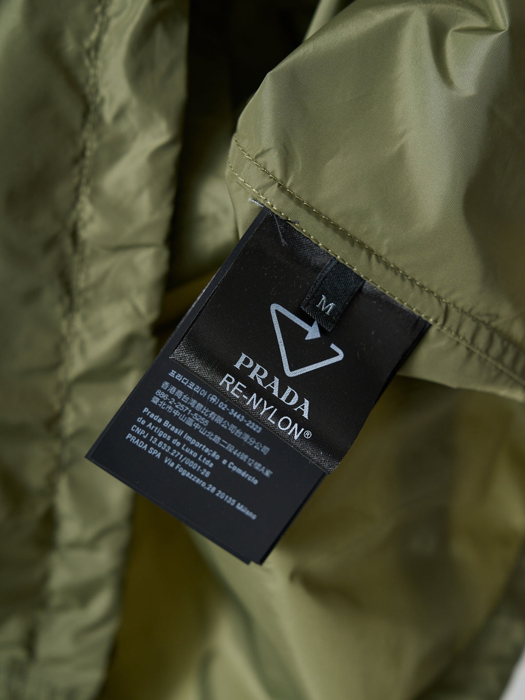 Prada Re-Nylon garment tag on olive green jacket fabric