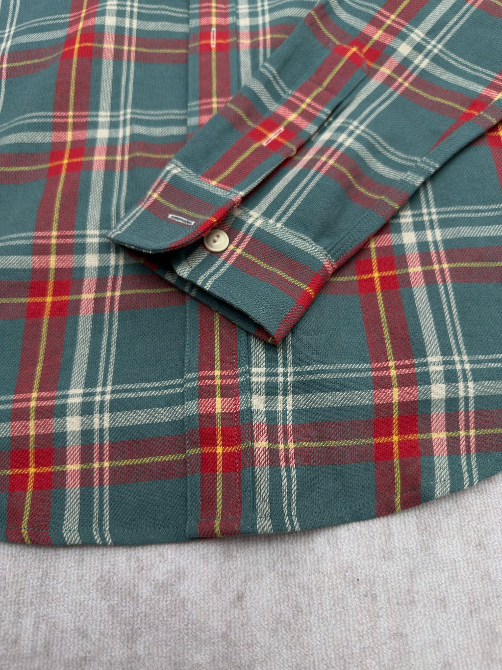Placket and cuff detail on teal plaid button-up shirt with round button