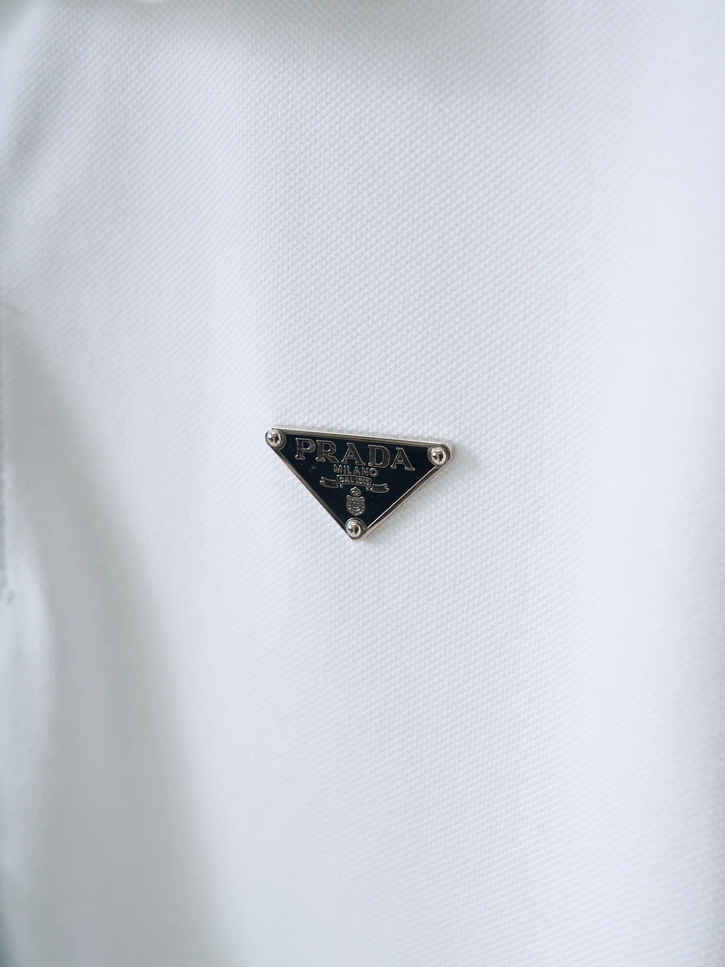 PRADA triangle logo on white polo shirt fabric