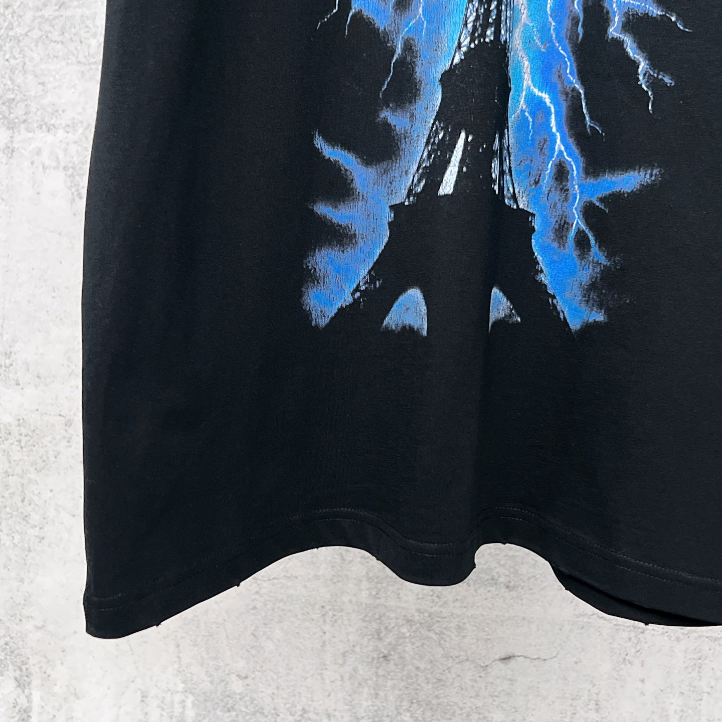 Black T-shirt hem with blue lightning Eiffel graphic near bottom