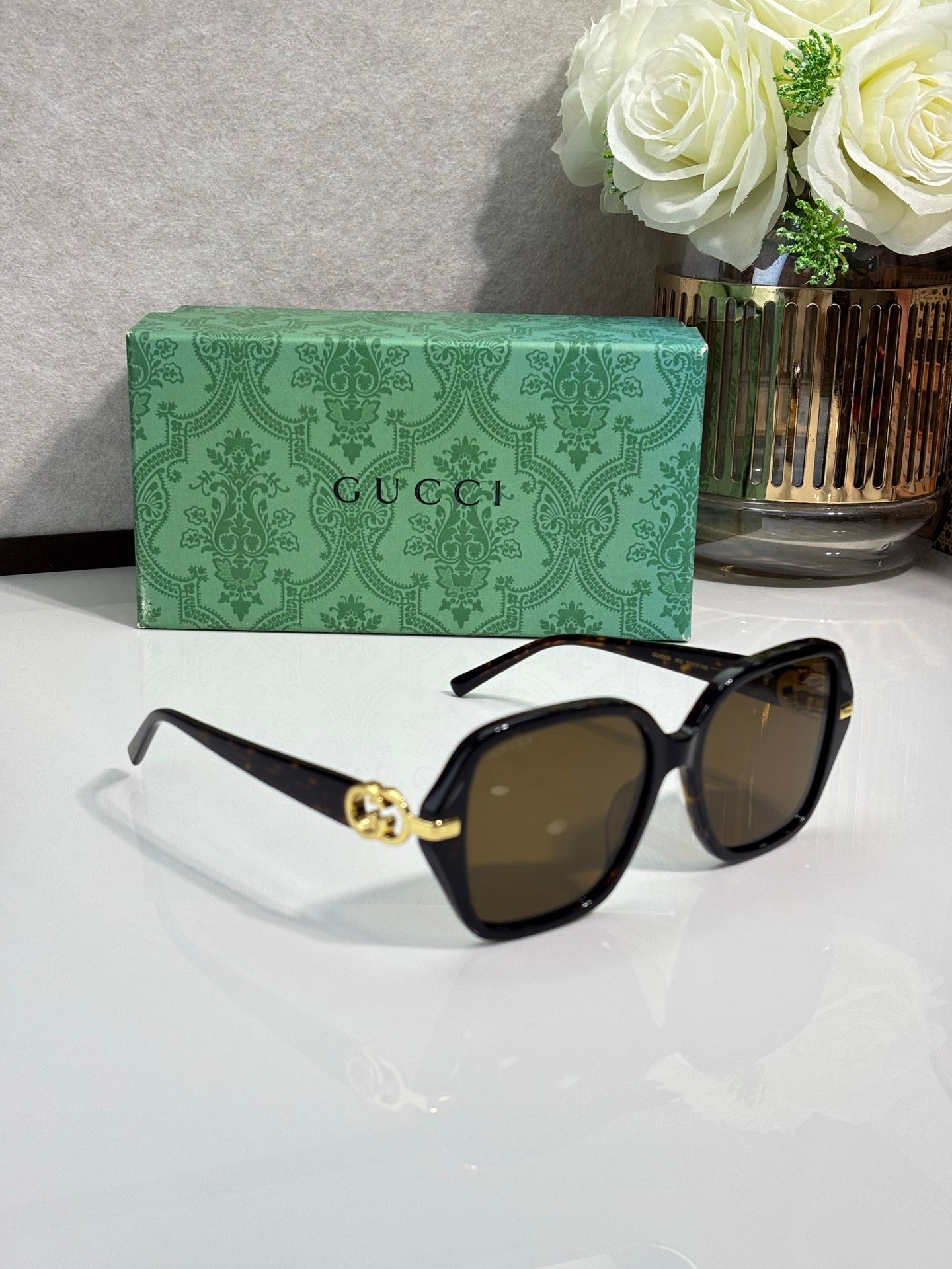 Gucci sunglasses with black square frames and brown tinted lenses, gold logo bridge