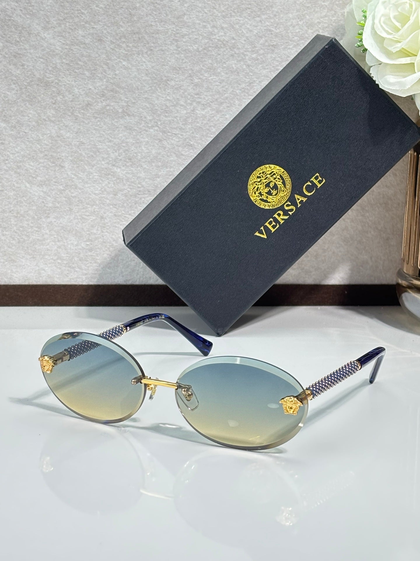 Versace sunglasses: round light frames, pale blue lenses, gold-tone temples.
