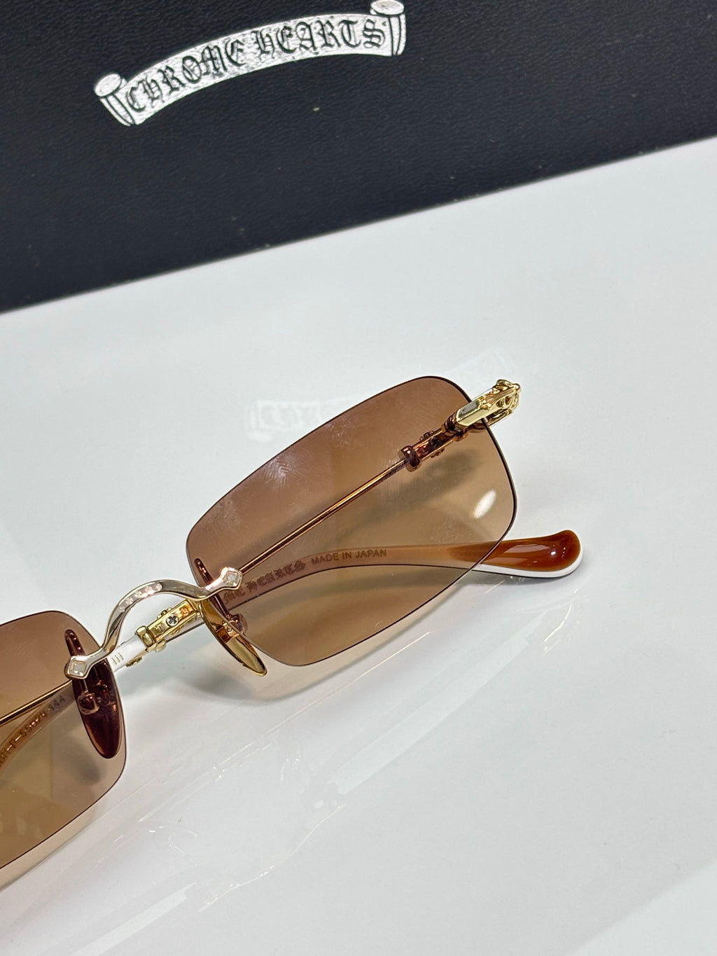 Close-up of gold metal eyeglasses with brown gradient lenses and ornate temple detail.