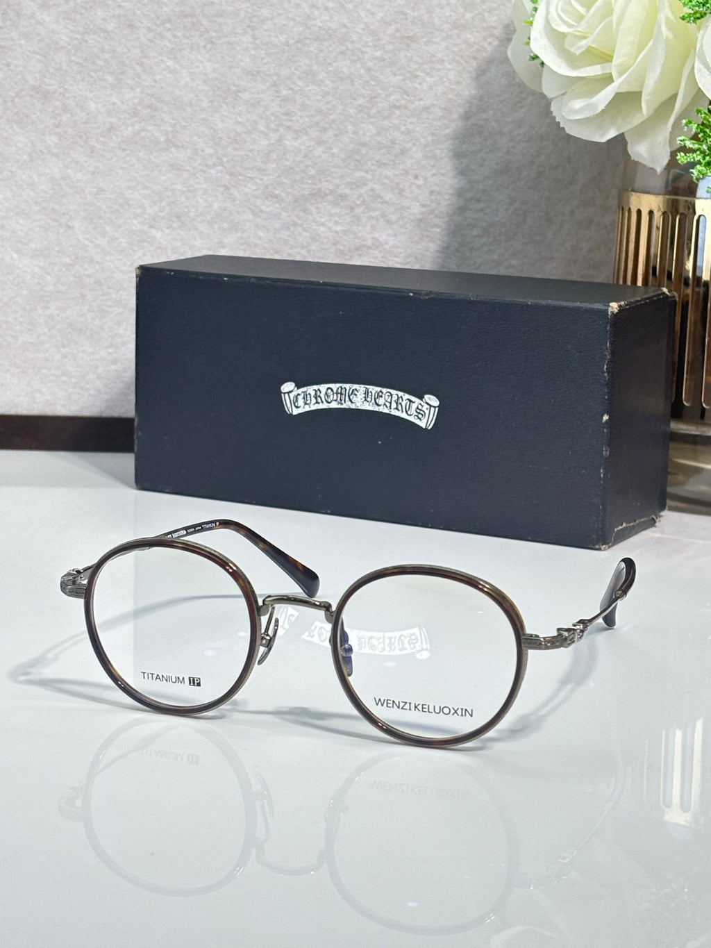 Round metal eyeglasses with dark frames and clear lenses, gold temple accents.