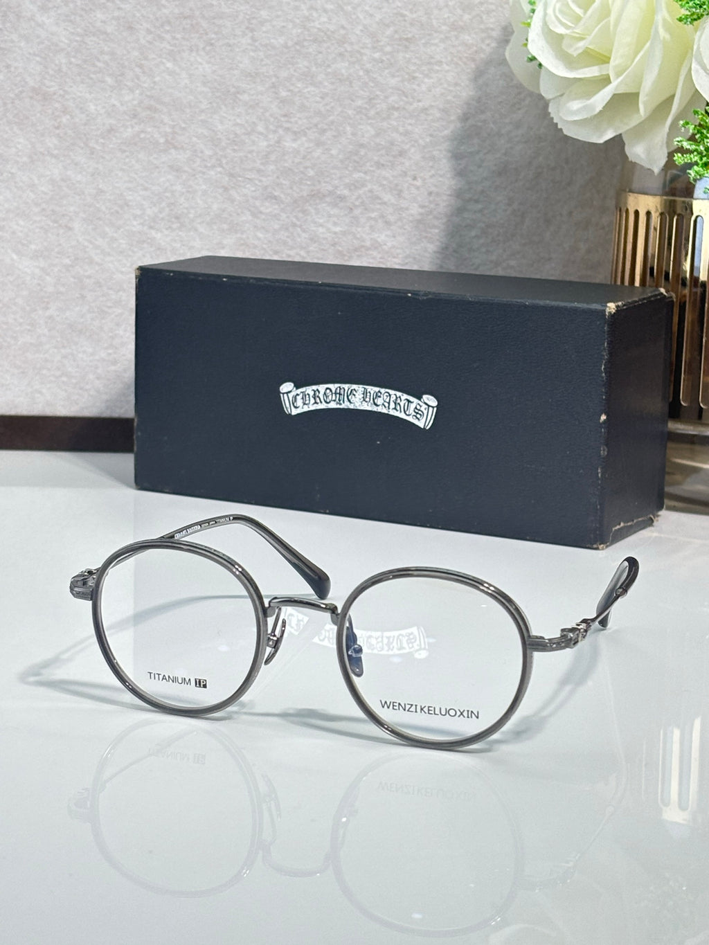 Round eyeglasses with dark metal rims and clear lenses, gold-detail arms.