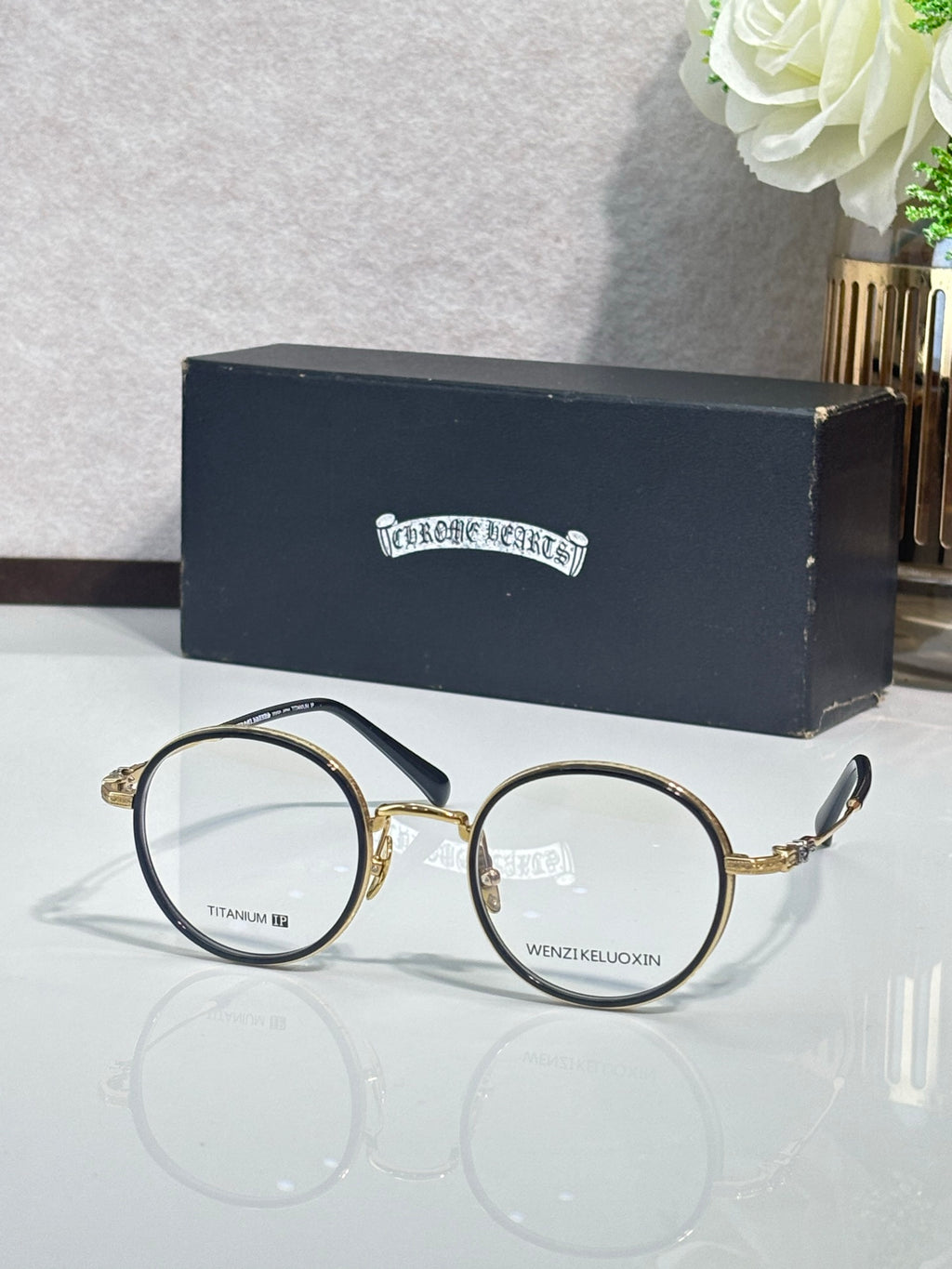 Round metal glasses with dark frames and clear lenses, gold hinge accents.