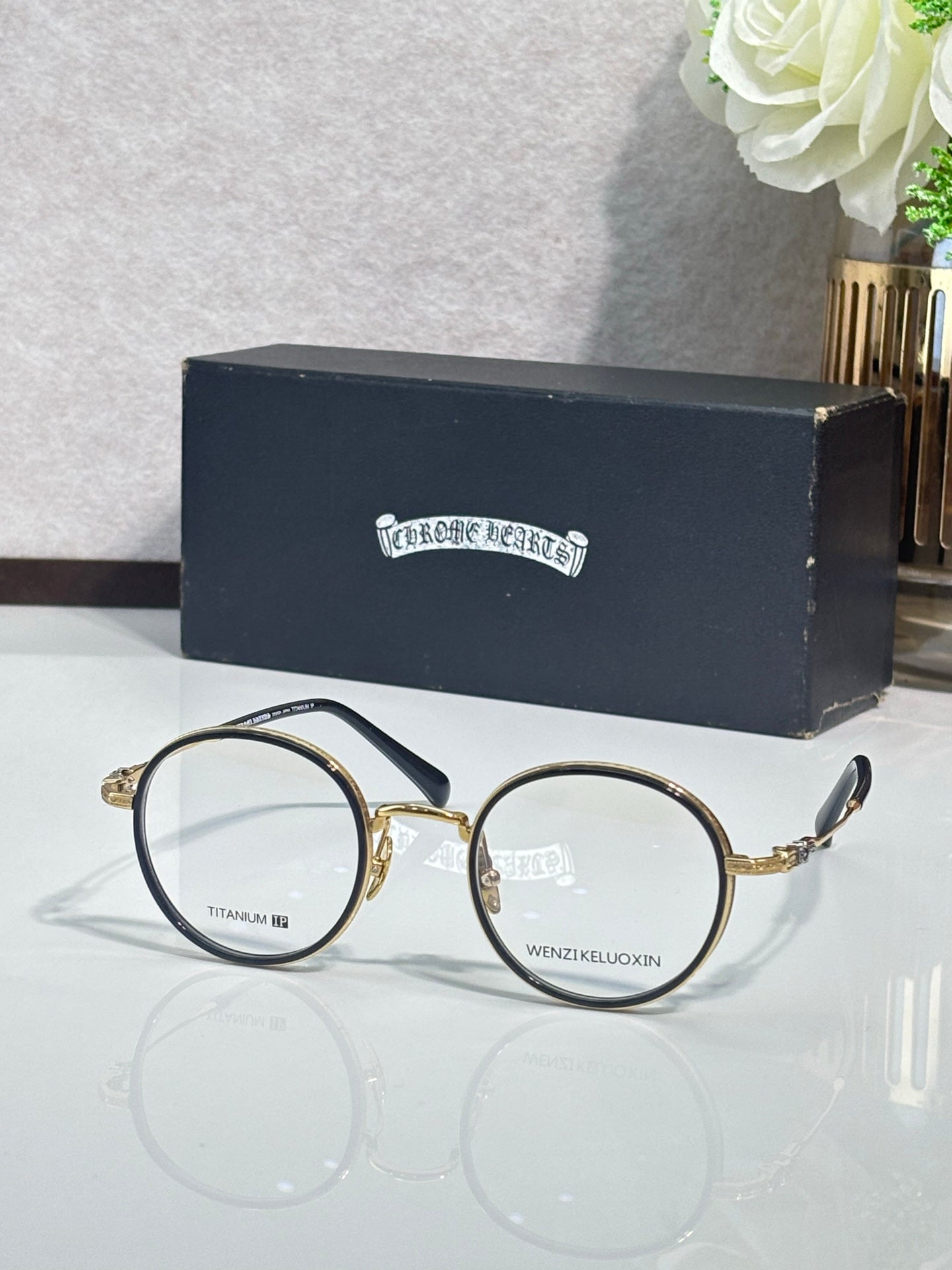 Round metal glasses with dark frames and clear lenses, gold hinge accents.