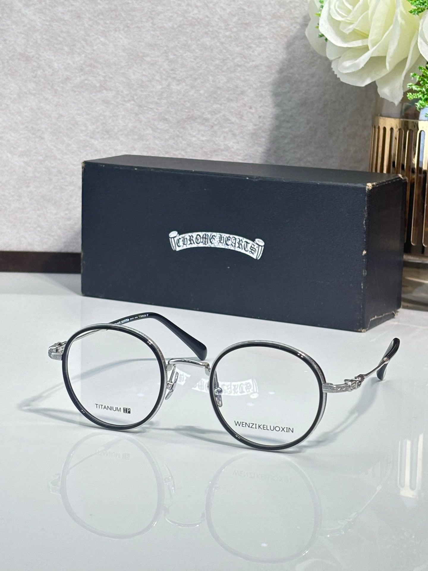 Round dark metal eyeglasses with clear lenses and curved arms, gold hardware.