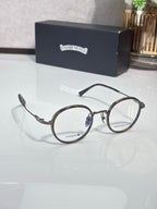 Round eyeglasses with dark frames, clear lenses, and gold-toned decorative temples.