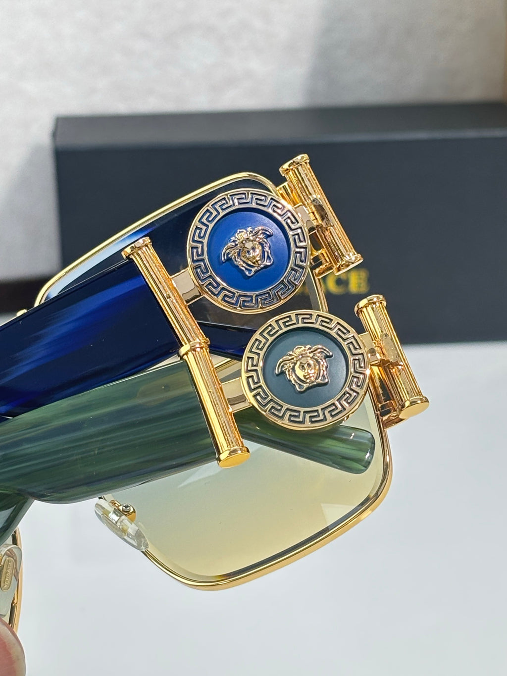 Gold eyeglass temple detail with blue and gold patterned emblem and hinge