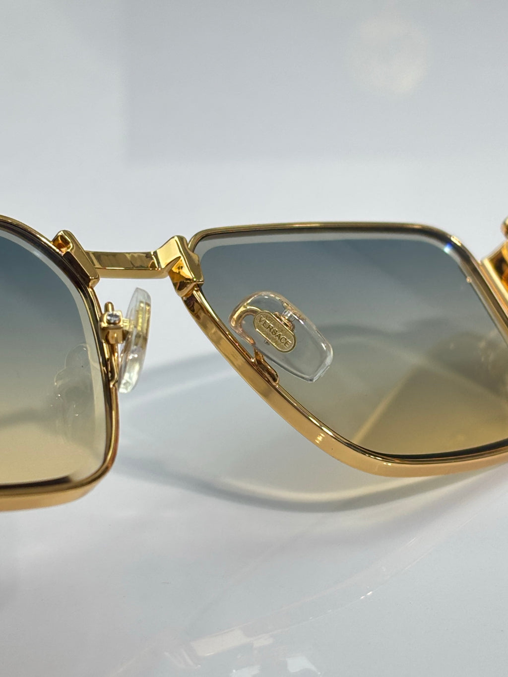 Gold-tone eyeglass frame close-up with blue-tinted lenses and engraved temple joint