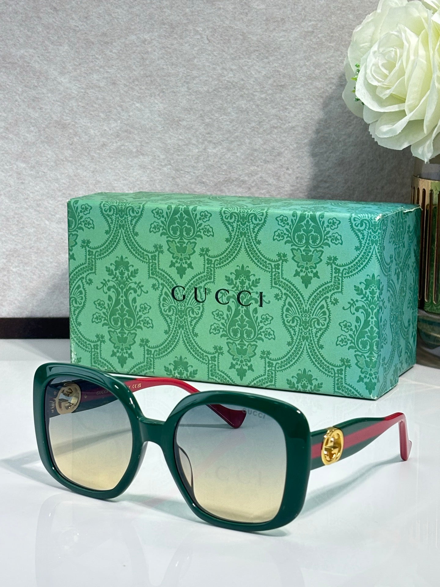 Gucci sunglasses with light lenses, dark green frame, red temple stripe and gold logo hardware.