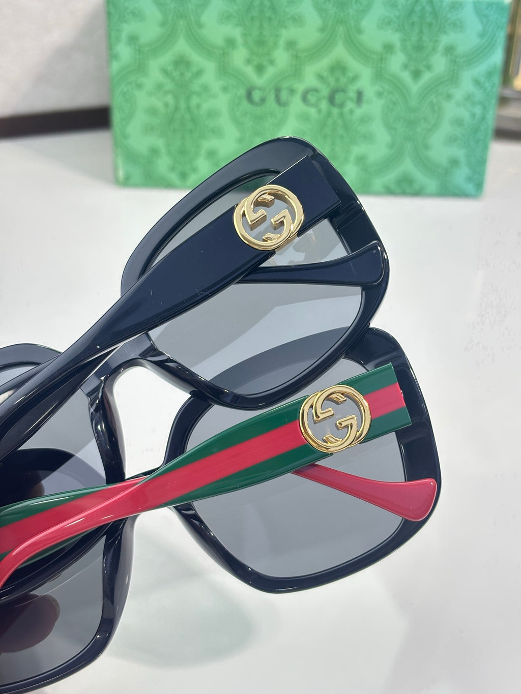 Gucci sunglasses close-up, temples with red-and-green stripe and gold GG hardware.