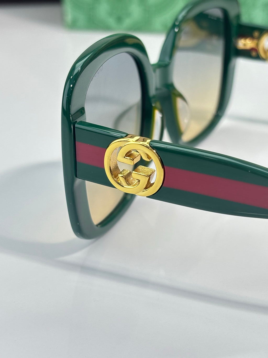 Gucci sunglasses close-up, green frame hinge with gold GG logo hardware.