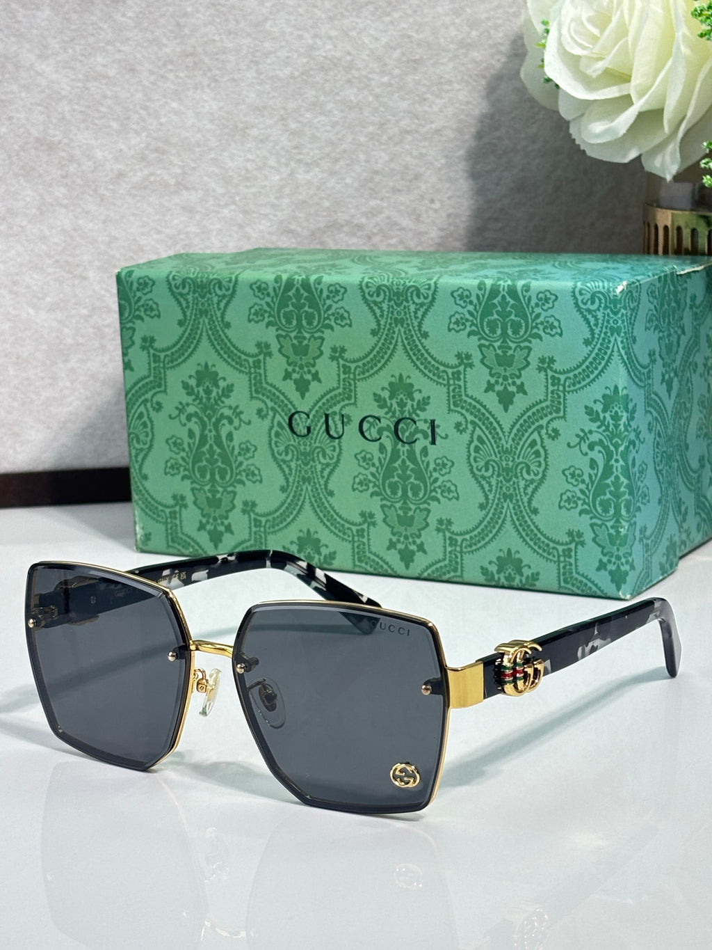 Gucci sunglasses with black square frames, dark gray lenses, and gold logo accents