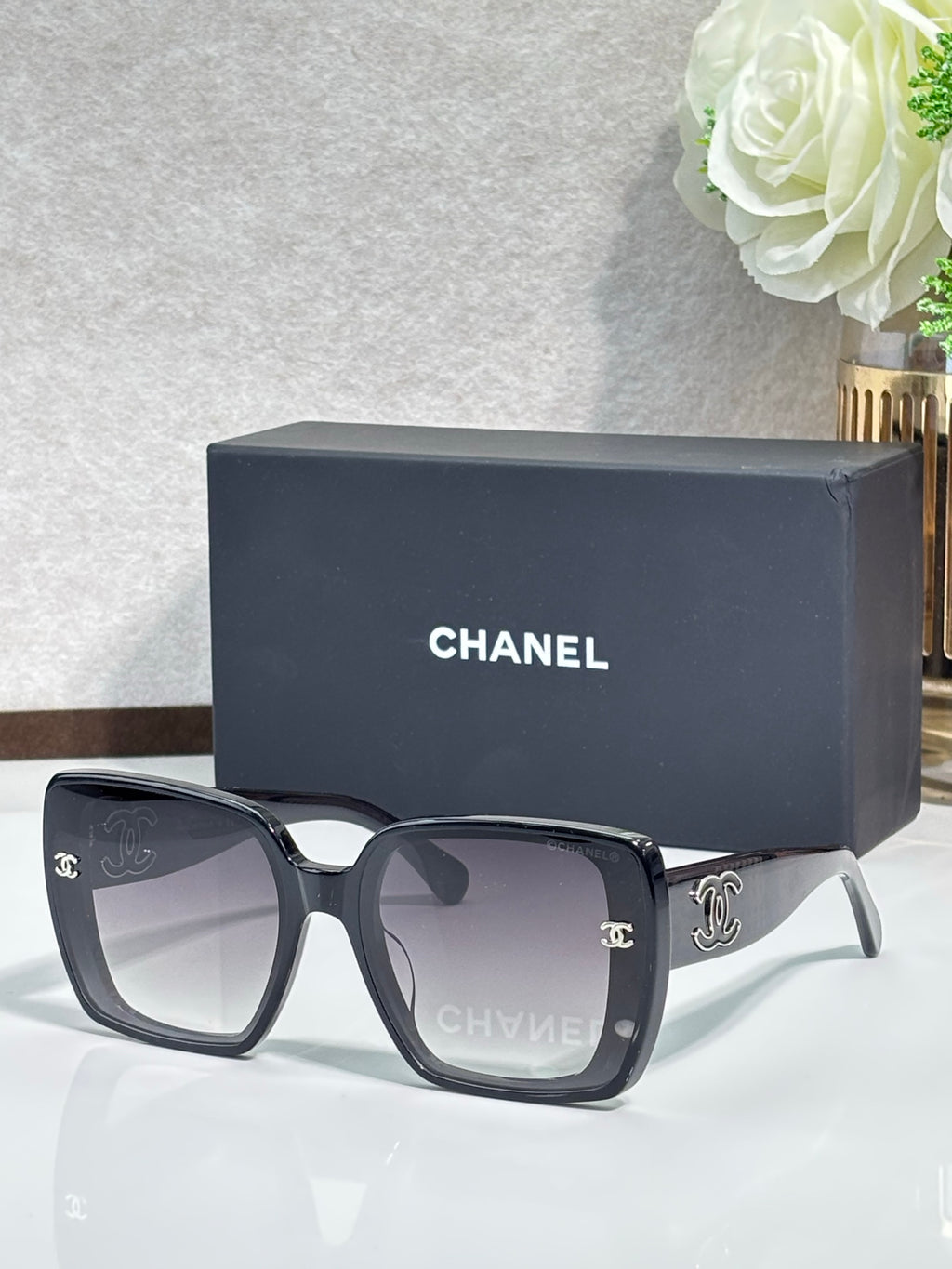 Chanel sunglasses with black square frames, gold CC logos, and dark lenses