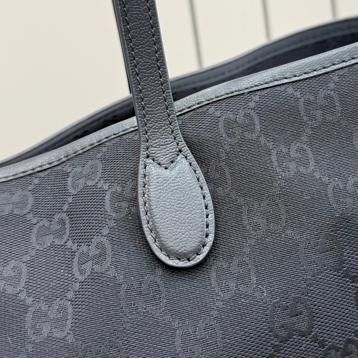 Gucci tote bag handle attachment close-up with dark gray stitched leather trim