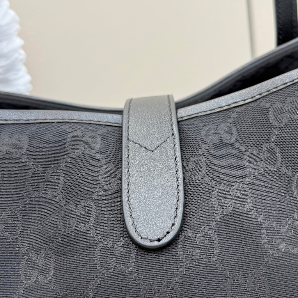 Gucci tote bag strap close-up with light gray leather tab and stitched edge