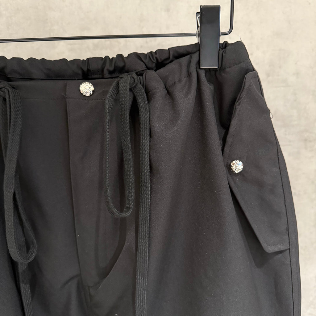 Black elastic-waist pants with front pocket, drawstring cords, and side flap pocket
