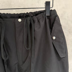 Black elastic-waist pants with front pocket, drawstring cords, and side flap pocket