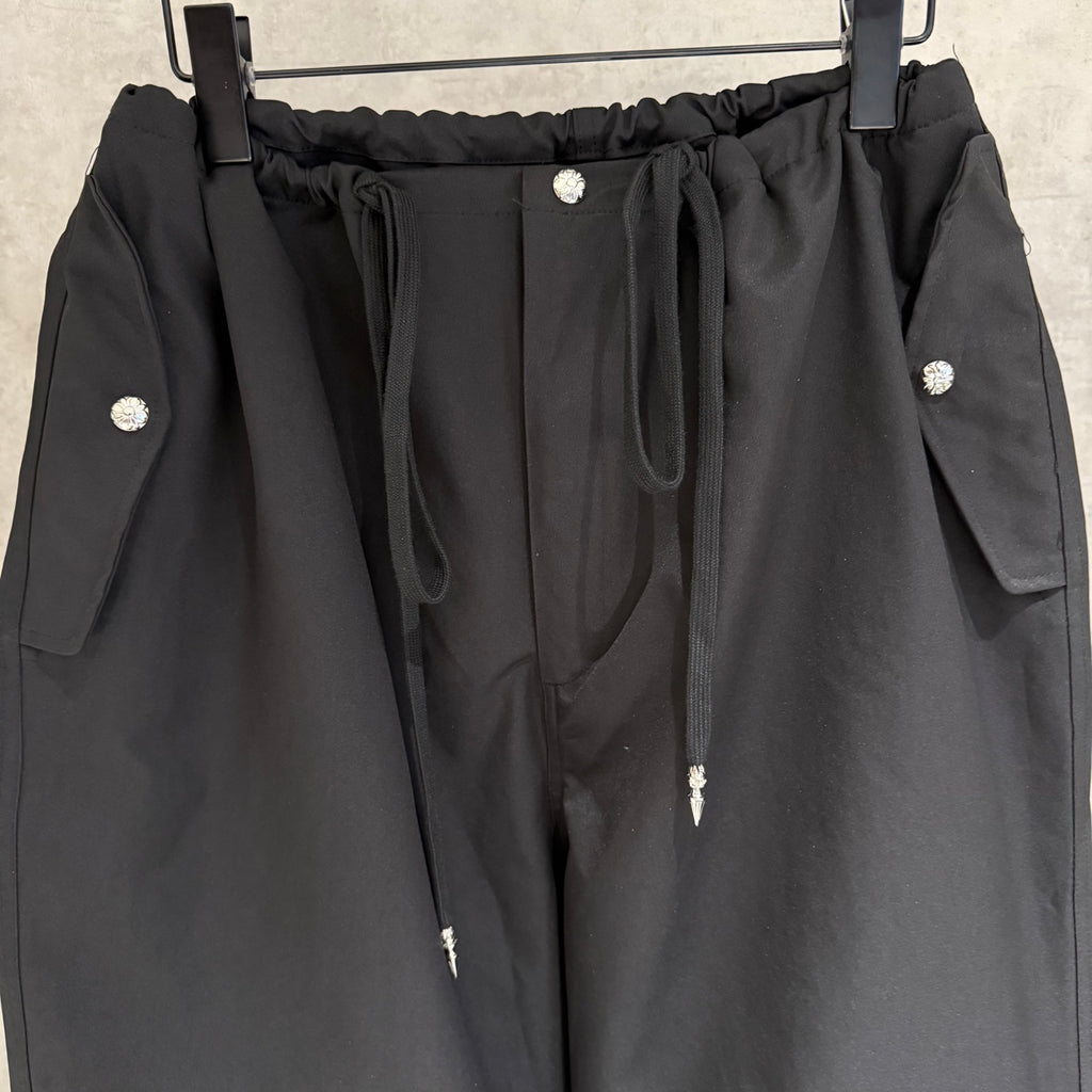 Black elastic-waist pants with front drawstring, snap buttons, and side pocket flaps