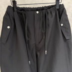 Black elastic-waist pants with front drawstring, snap buttons, and side pocket flaps