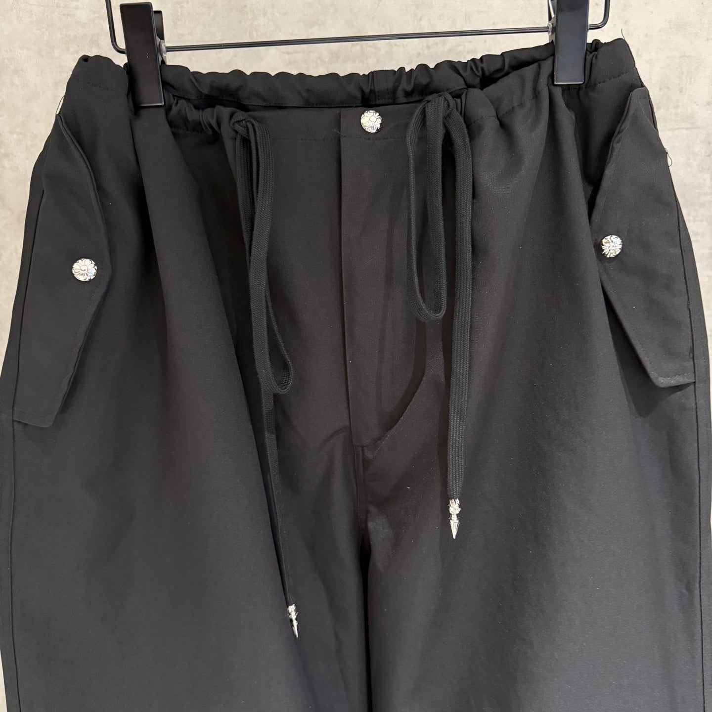 Black elastic-waist pants with front drawstring, snap buttons, and side pocket flaps