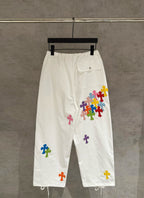 White cargo pants with elastic waist, drawstring, and multicolor cross appliques